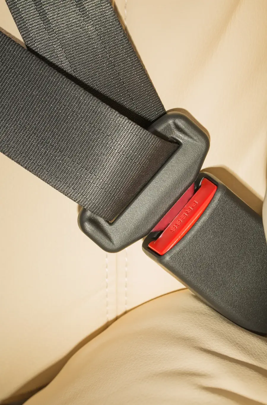 Seat belt assembly fastened across a light-coloured vehicle seat, showing webbing entering the buckle housing