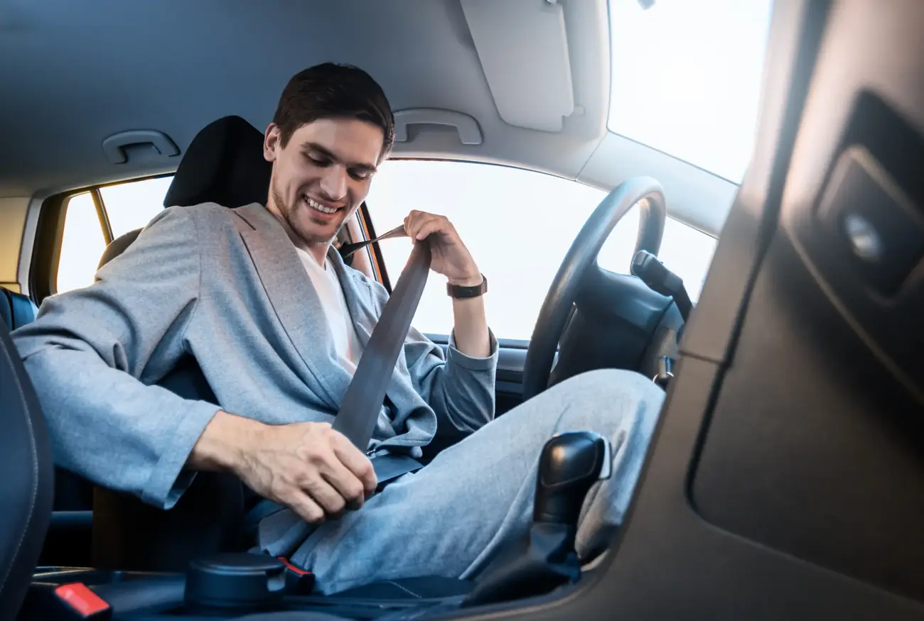 Driver drawing the seat belt across the shoulder in a passenger car before setting off