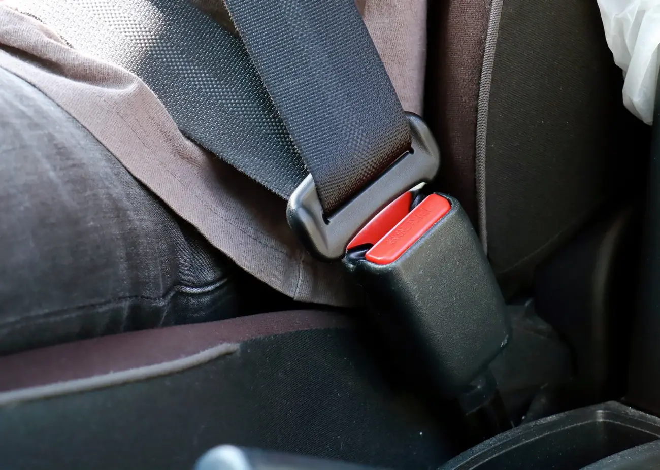 Metal seat belt tongue plate held next to its buckle housing inside a vehicle