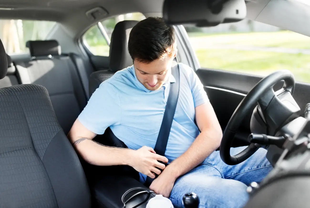 Driver fastening a three-point seat belt in a passenger car interior