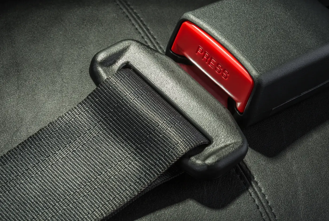 Seat belt tongue plate fully engaged inside its buckle housing, shown against dark automotive upholstery