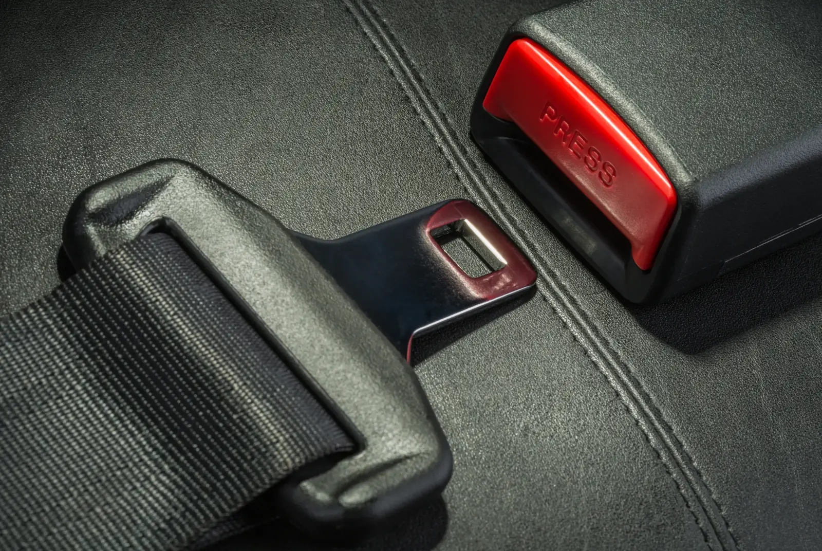 Seat belt buckle housing with red release button beside a metal tongue plate on a dark trim surface