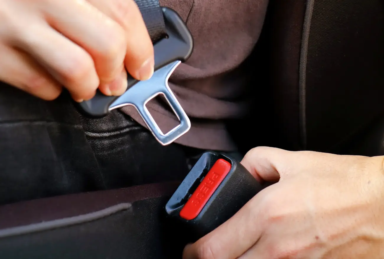 Hands bringing a seat belt tongue plate towards the buckle housing inside a vehicle